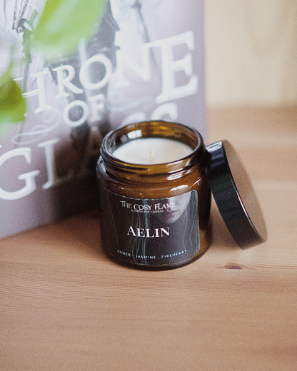 Amber glass candle jar labelled ‘Aelin’ from The Cosy Flame, scented with amber and jasmine, and Throne of Glass book in the background.