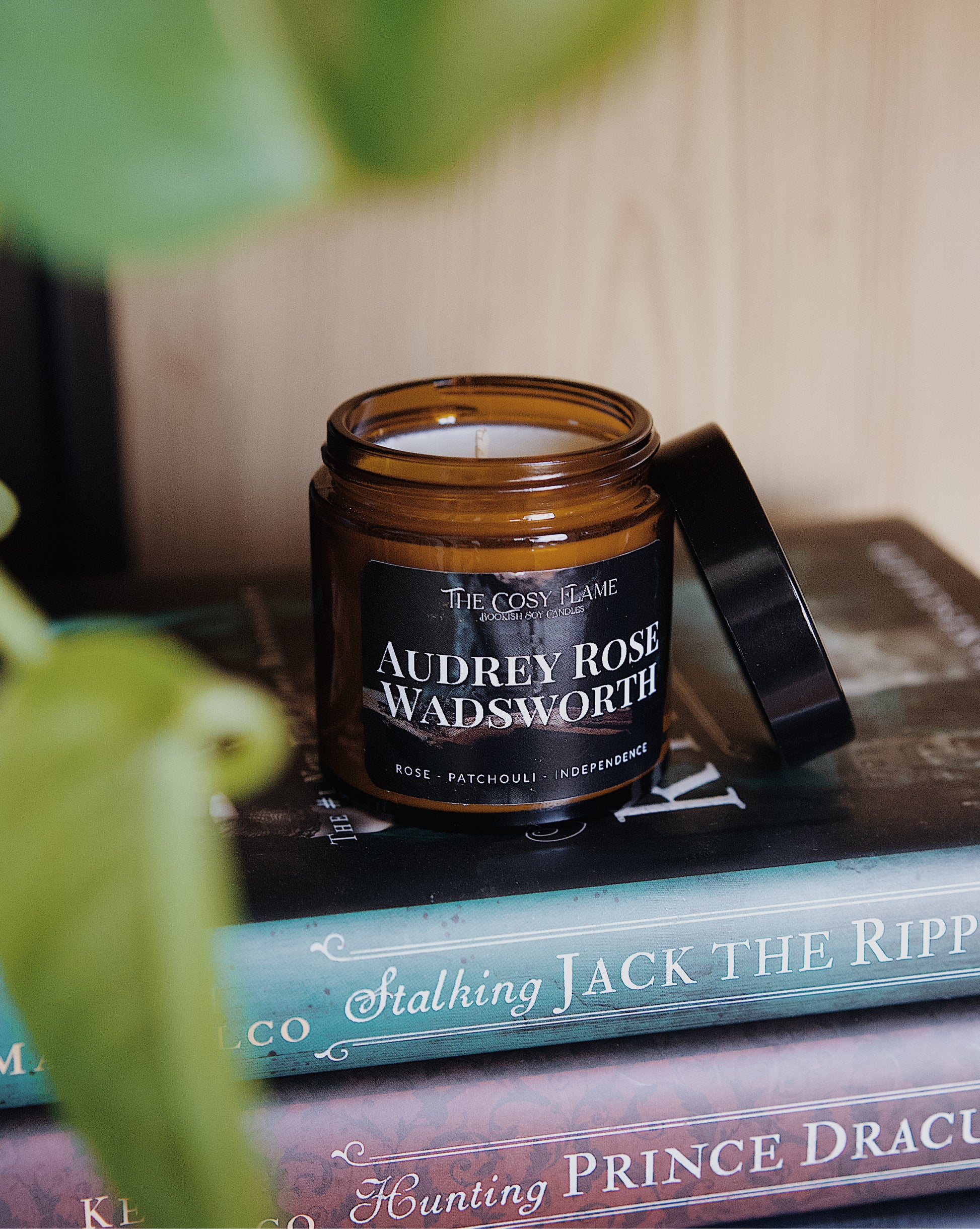 Amber glass candle jar labelled ‘Audrey Rose Wadsworth’ from The Cosy Flame, scented with rose and patchouli, and Stalking Jack the Ripper books in the background.