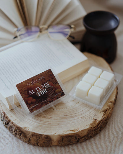 Autumn TBR soy wax melts by The Cosy Flame, featuring pumpkin spice and cinnamon scent notes, displayed on a wooden slice beside an open book and glasses.