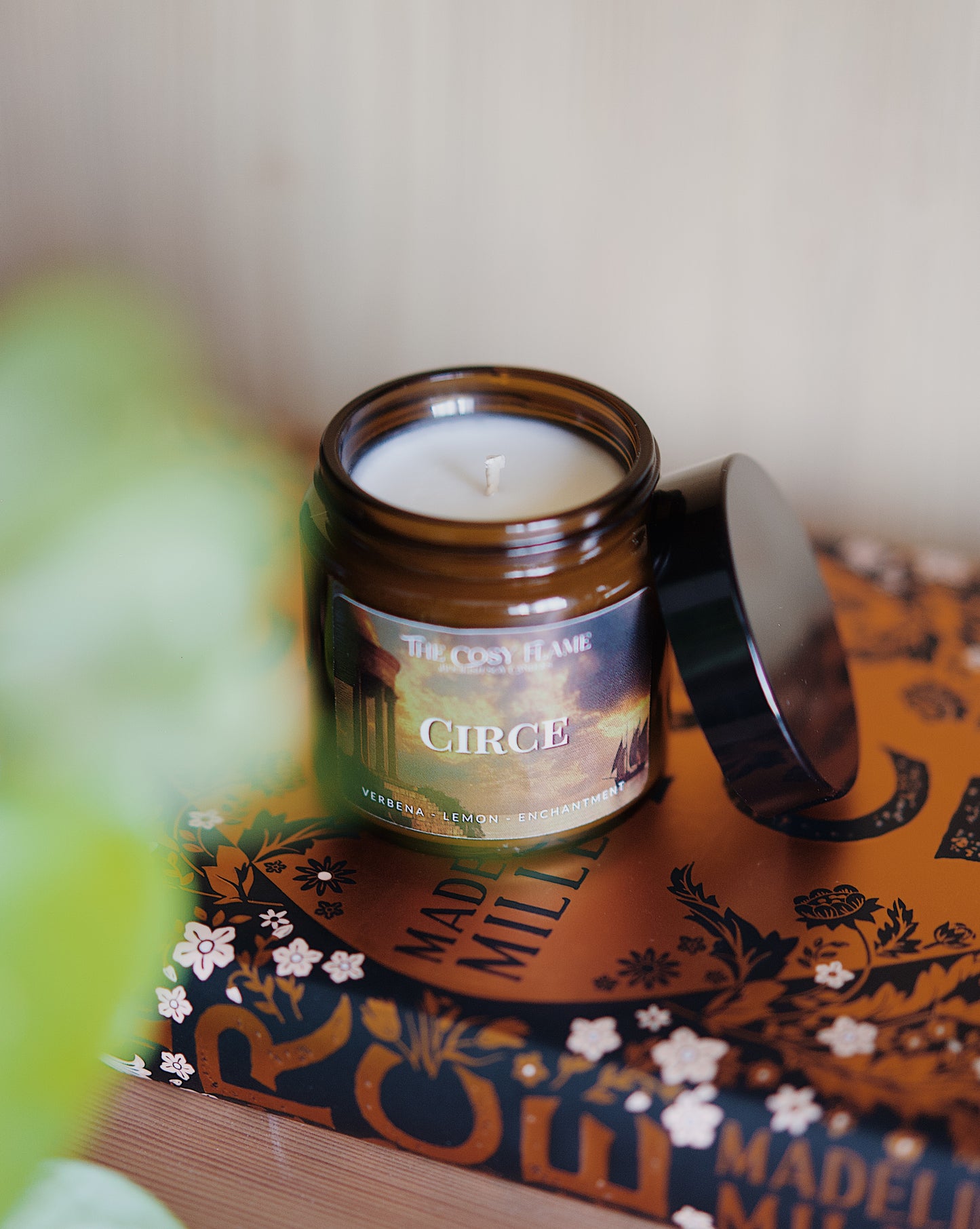 Amber glass candle jar labelled ‘Circe’ from The Cosy Flame, scented with verbena and lemon, and Circe book in the background.