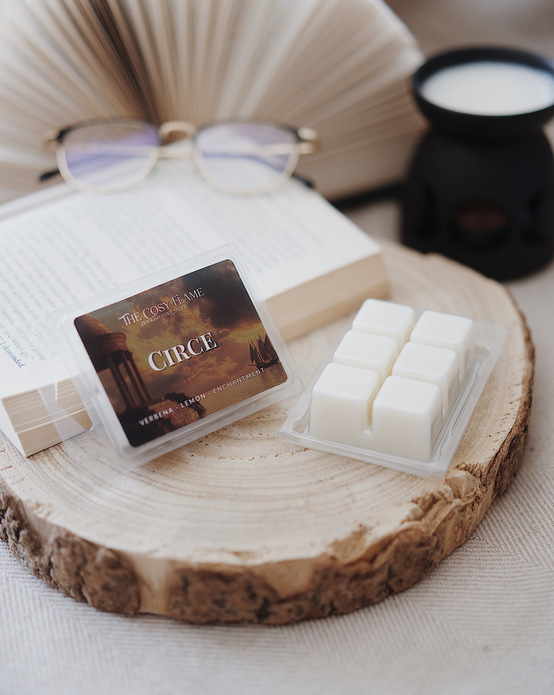 Circe soy wax melts by The Cosy Flame, featuring verbena and lemon scent notes, displayed on a wooden slice beside an open book and glasses.