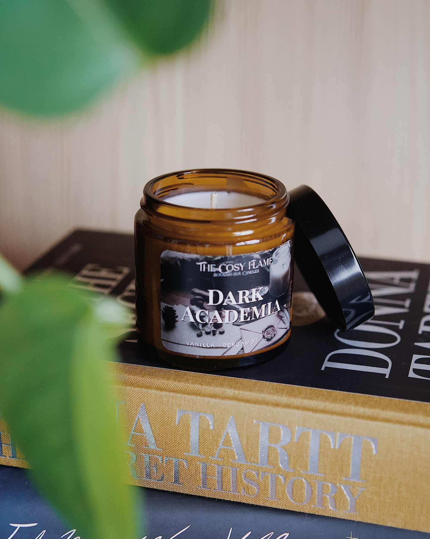 Amber glass candle jar labelled ‘Dark Academia’ from The Cosy Flame, scented with vanilla and bergamot, and The Secret History book in the background.