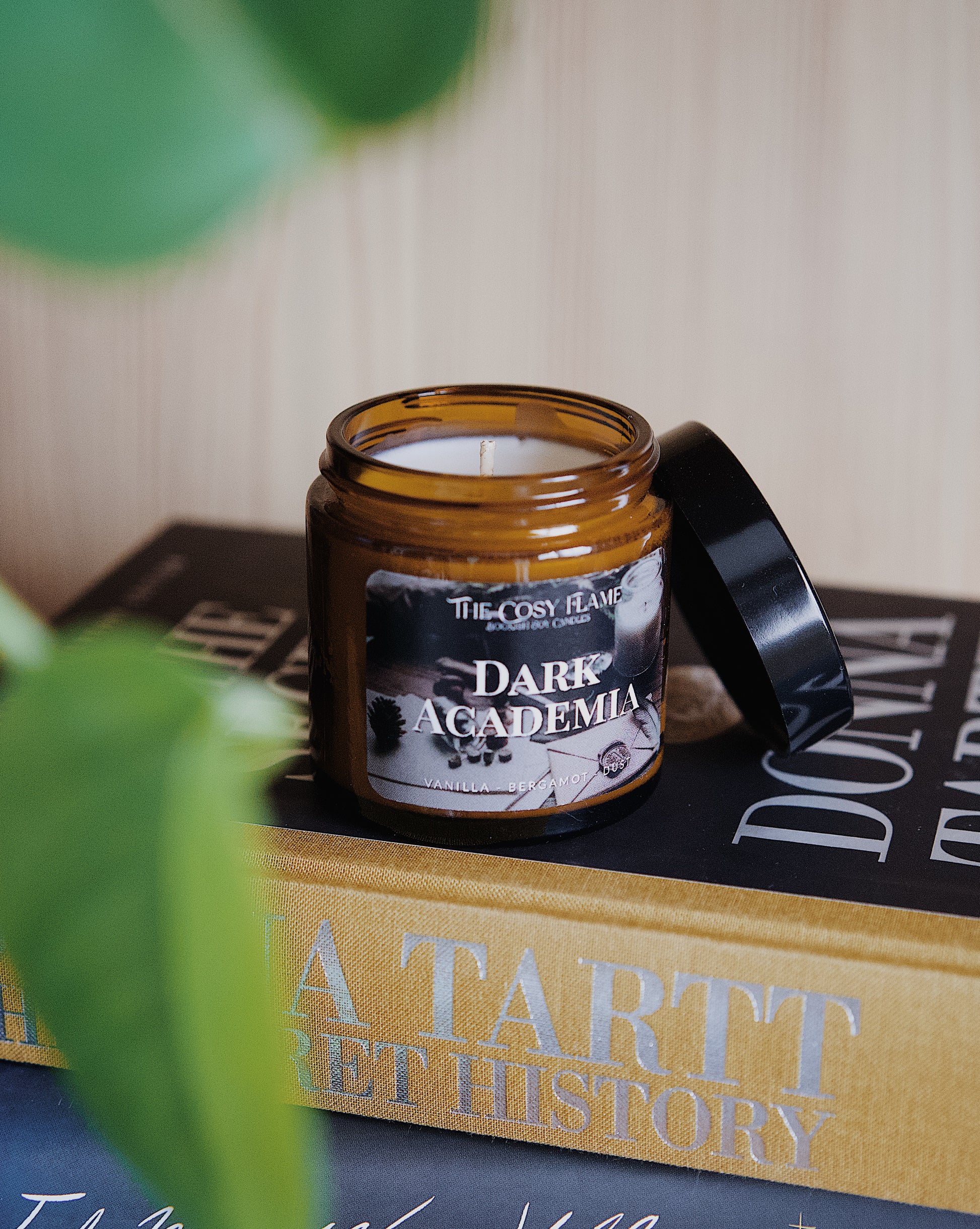 Amber glass candle jar labelled ‘Dark Academia’ from The Cosy Flame, scented with vanilla and bergamot, and The Secret History book in the background.