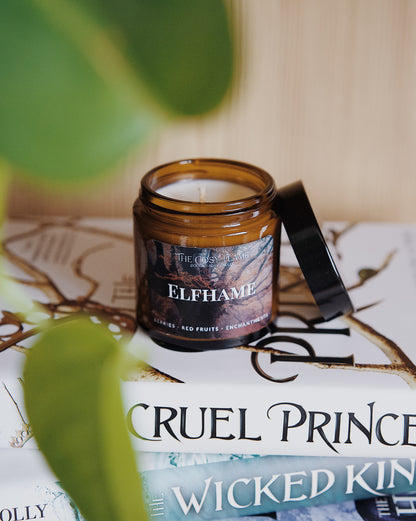 Amber glass candle jar labelled ‘Elfhame’ from The Cosy Flame, scented with berries and red fruits, and The Cruel Prince books in the background.