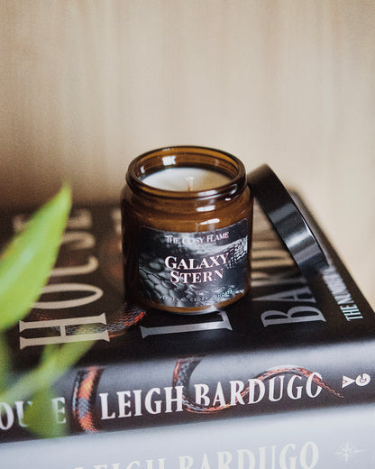 Amber glass candle jar labelled ‘Galaxy Stern’ from The Cosy Flame, scented with verbena and cedar, and Ninth House book in the background.
