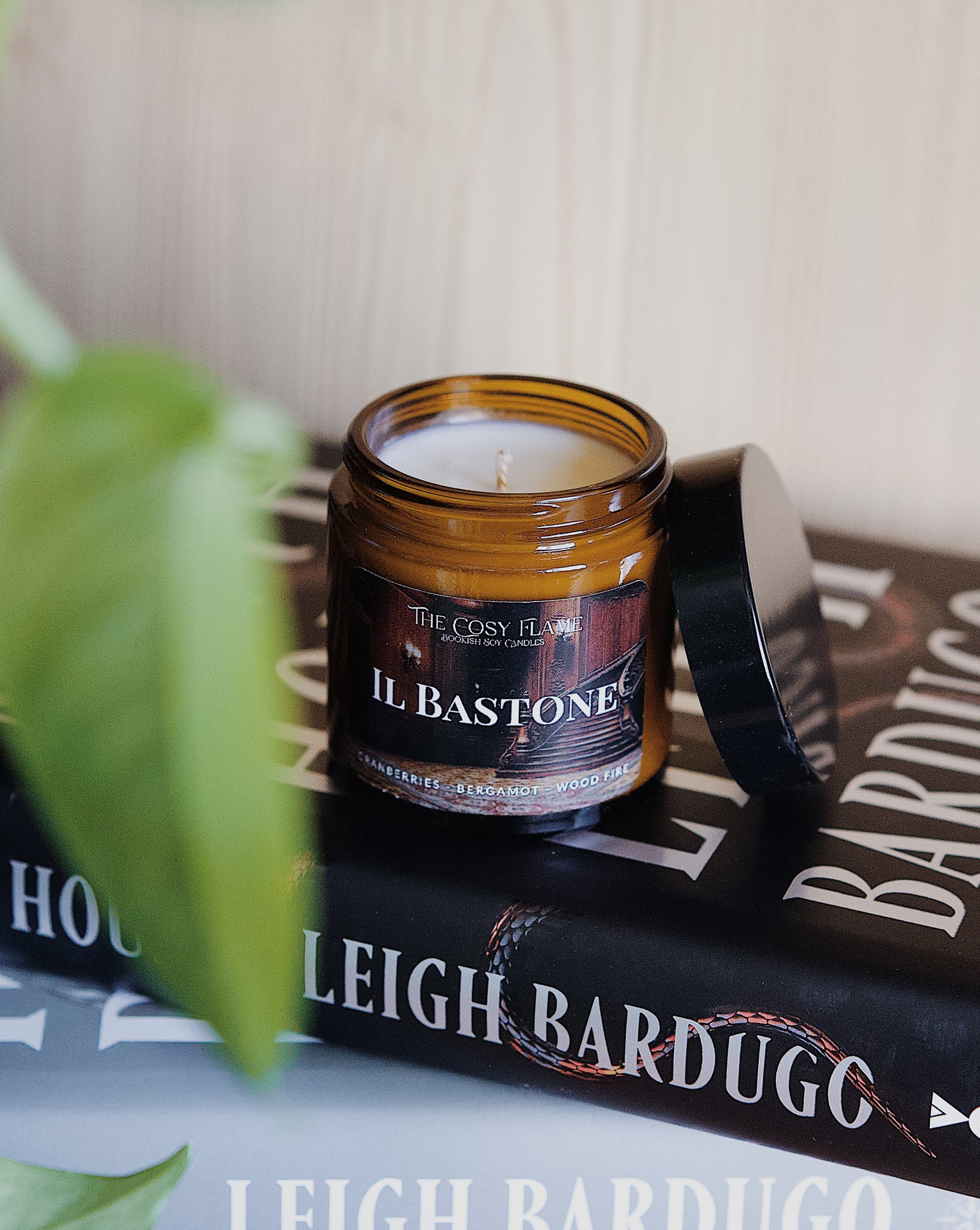 Amber glass candle jar labelled ‘Il Bastone’ from The Cosy Flame, scented with cranberries, bergamot and wood fire, and Ninth House book in the background.