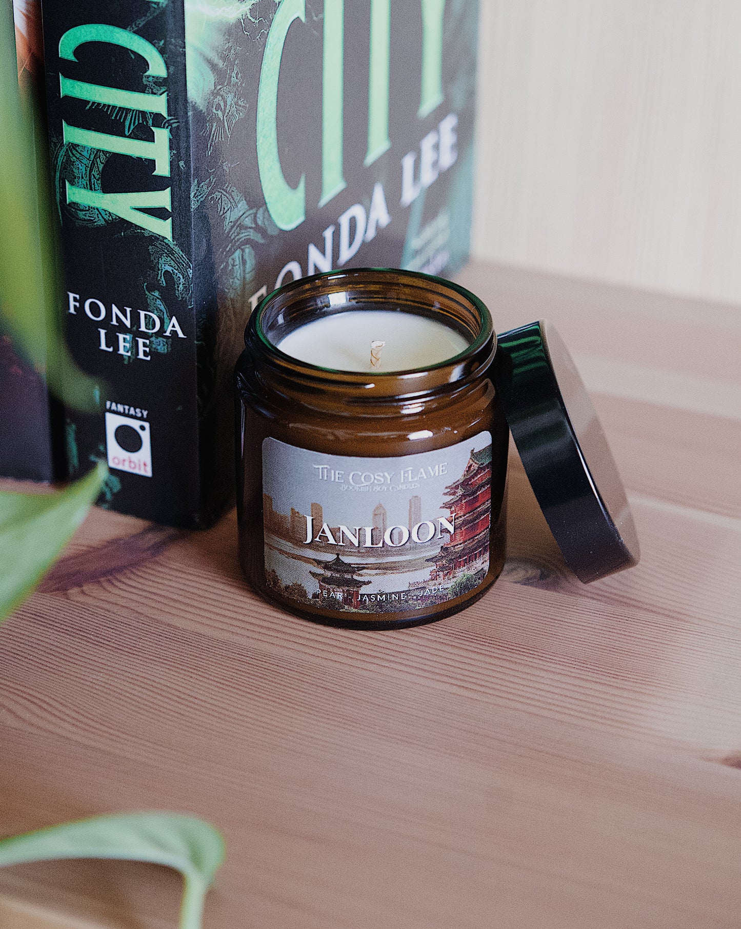 Amber glass candle jar labelled ‘Janloon’ from The Cosy Flame, scented with pear and jasmine, and Jade City book in the background.