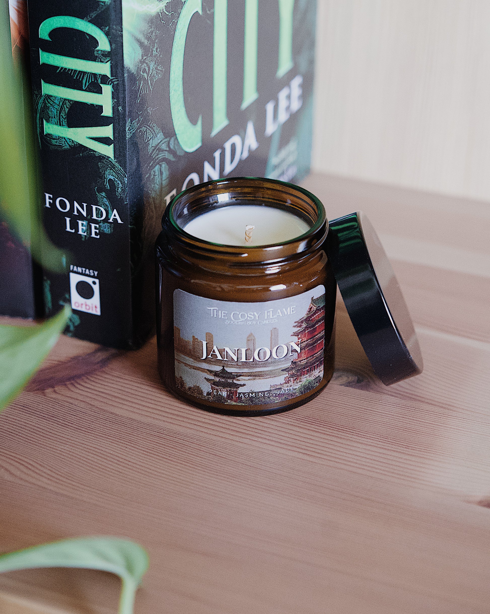 Amber glass candle jar labelled ‘Janloon’ from The Cosy Flame, scented with pear and jasmine, and Jade City book in the background.