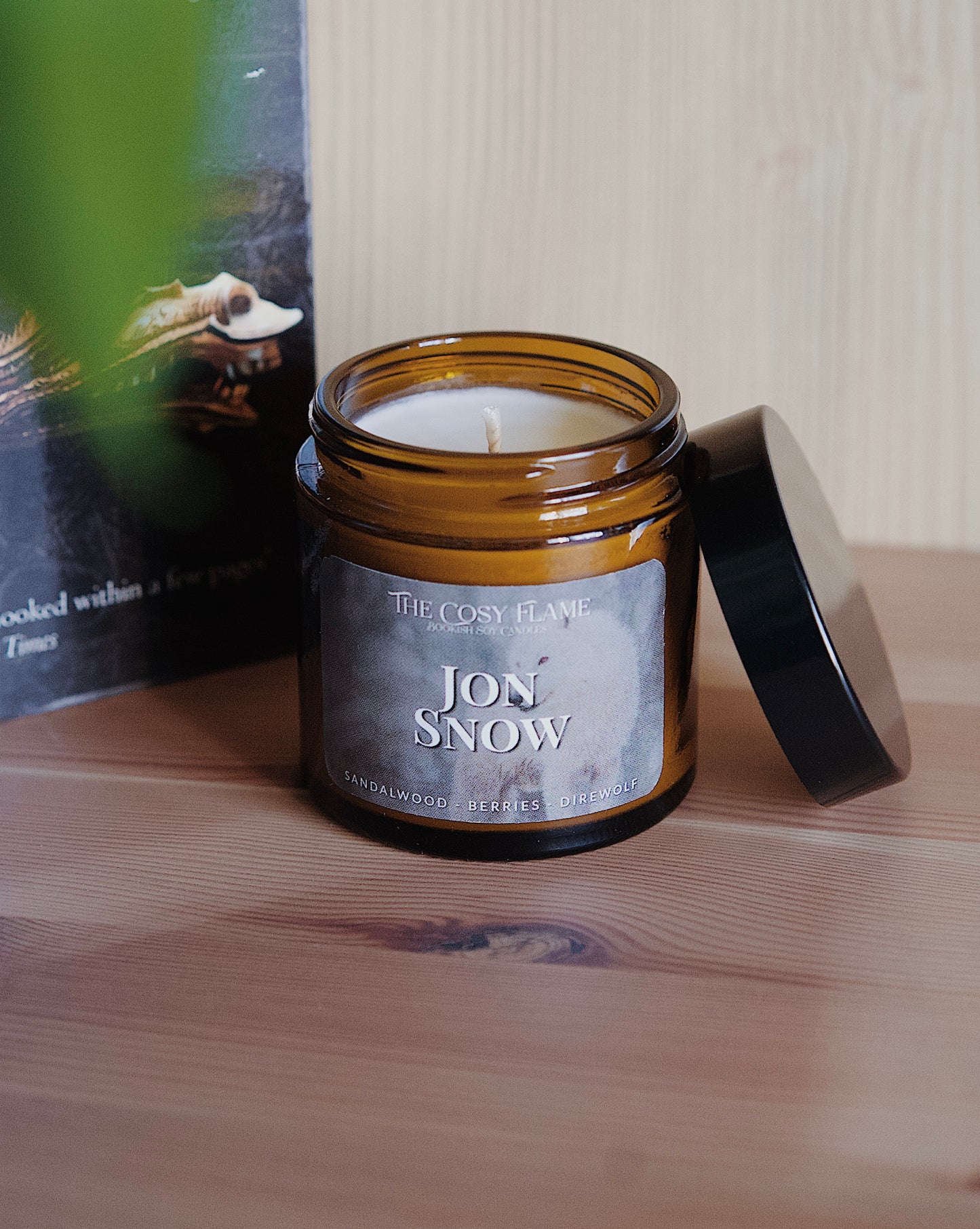 Amber glass candle jar labelled ‘Jon Snow’ from The Cosy Flame, scented with sandalwood and berries, and Game of Thrones book in the background.
