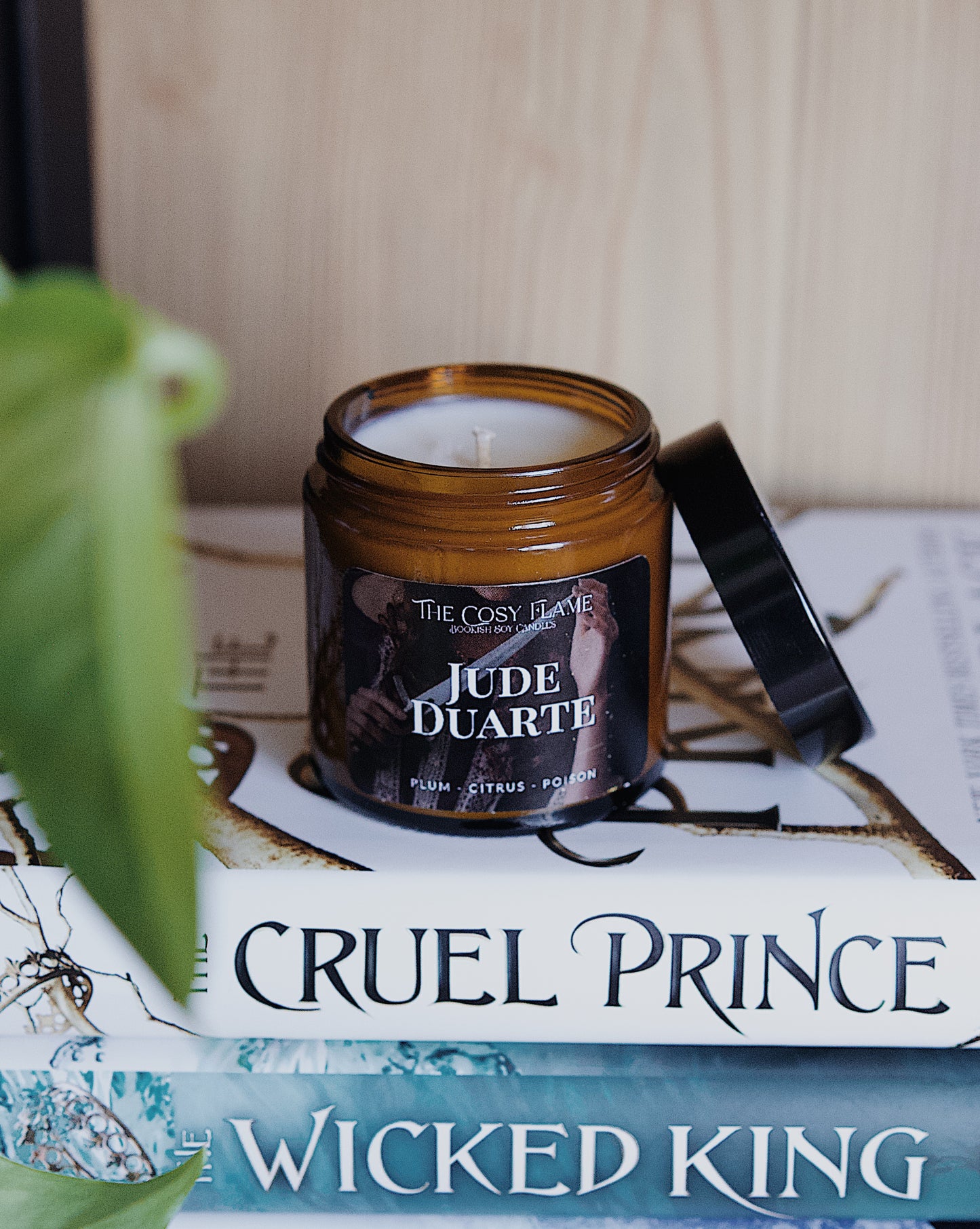 Amber glass candle jar labelled ‘Jude Duarte’ from The Cosy Flame, scented with plum and citrus, and The Cruel Prince books in the background.
