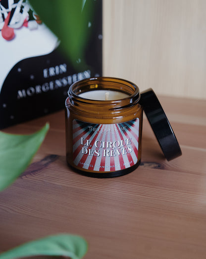Amber glass candle jar labelled ‘Le Cirque des Rêves’ from The Cosy Flame, scented with caramel and candy apple, and The Night Circus book in the background.