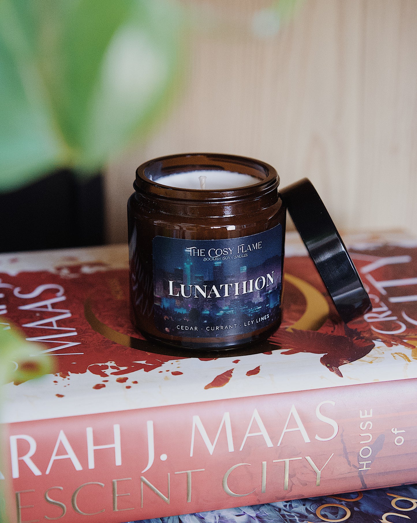 Amber glass candle jar labelled ‘Lunathion’ from The Cosy Flame, scented with cedar and currant, and Crescent City books in the background.