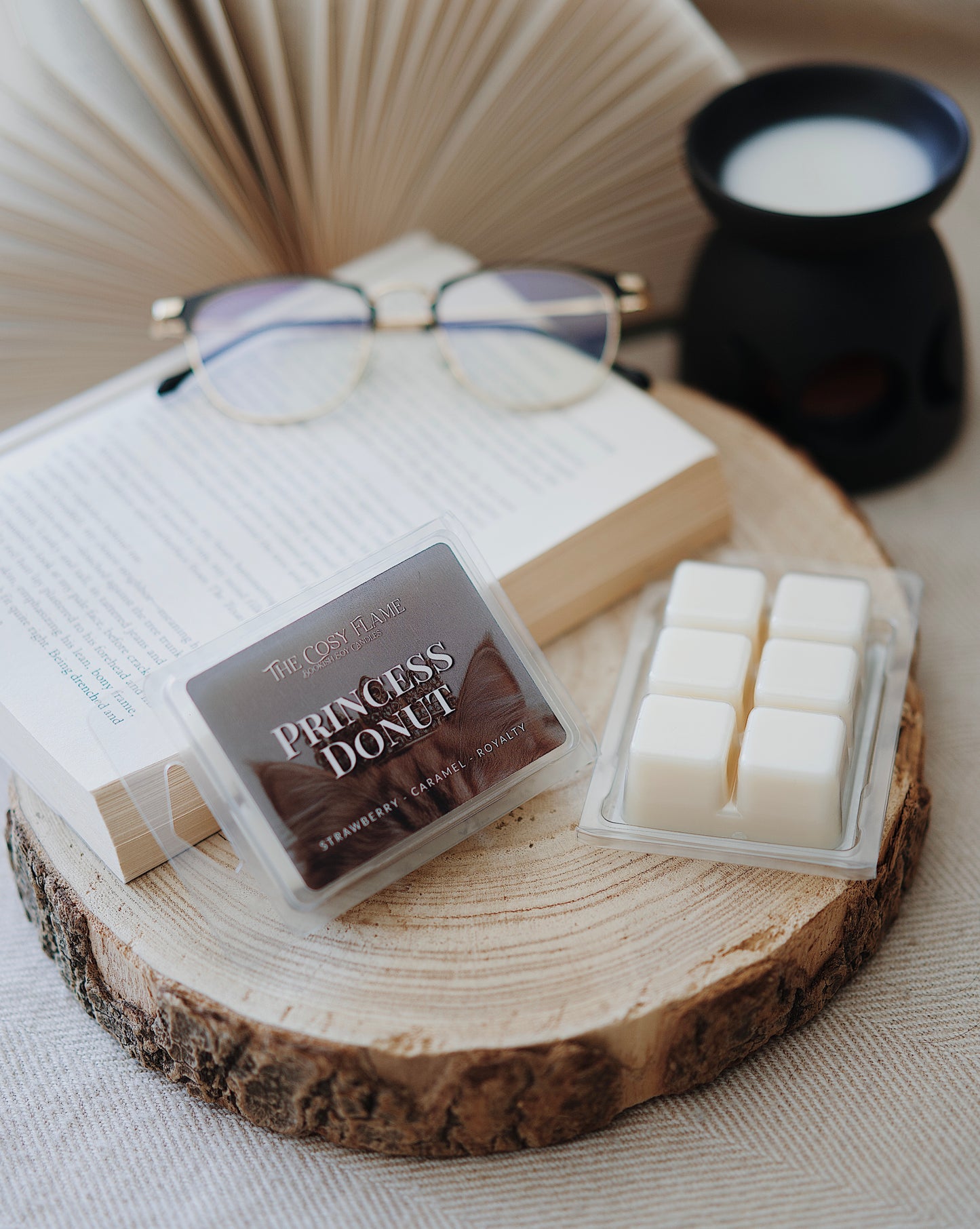 Princess Donut soy wax melts by The Cosy Flame, featuring strawberry and caramel scent notes, displayed on a wooden slice beside an open book and glasses.