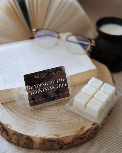 Reading by the Christmas Tree soy wax melts by The Cosy Flame, featuring orange and cinnamon scent notes, displayed on a wooden slice beside an open book and glasses.
