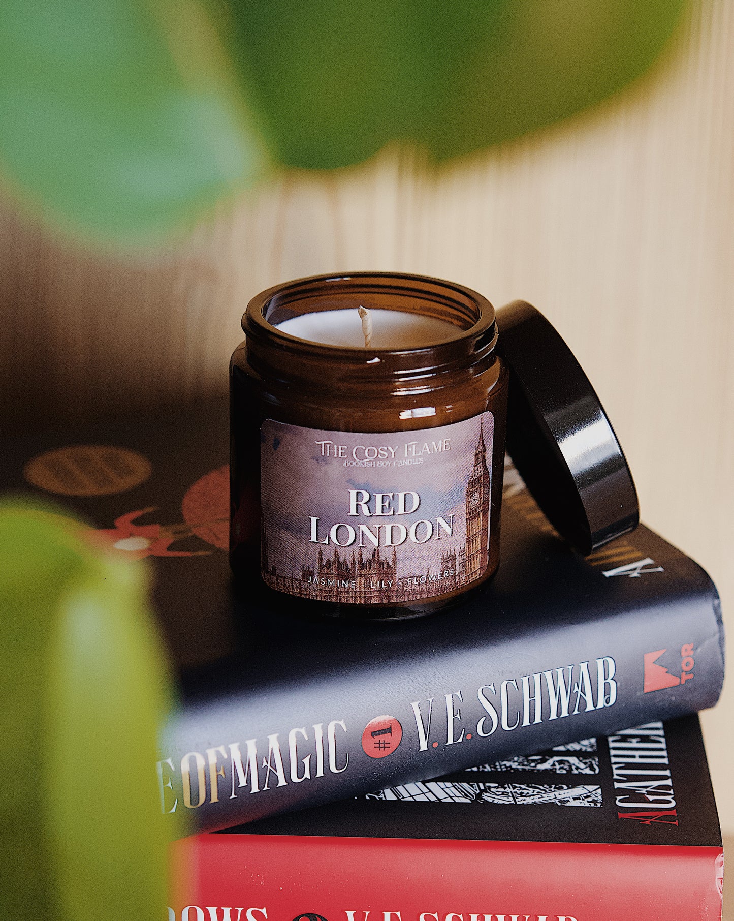 Amber glass candle jar labelled ‘Red London’ from The Cosy Flame, scented with jasmine and lily, and Shades of Magic books in the background.