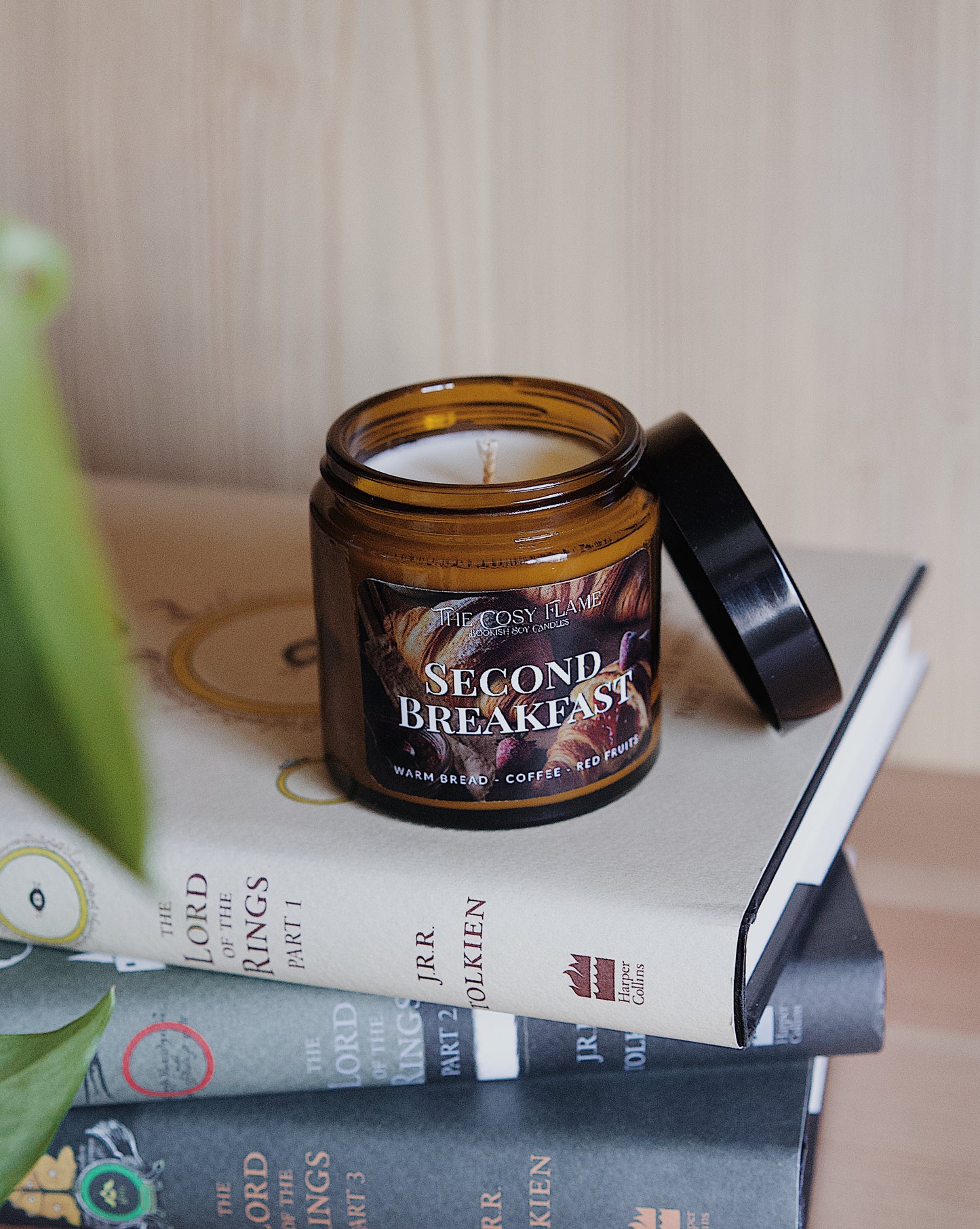 Amber glass candle jar labelled ‘Second Breakfast’ from The Cosy Flame, scented with warm bread, coffee and red fruits, and The Lord of the Rings books in the background.