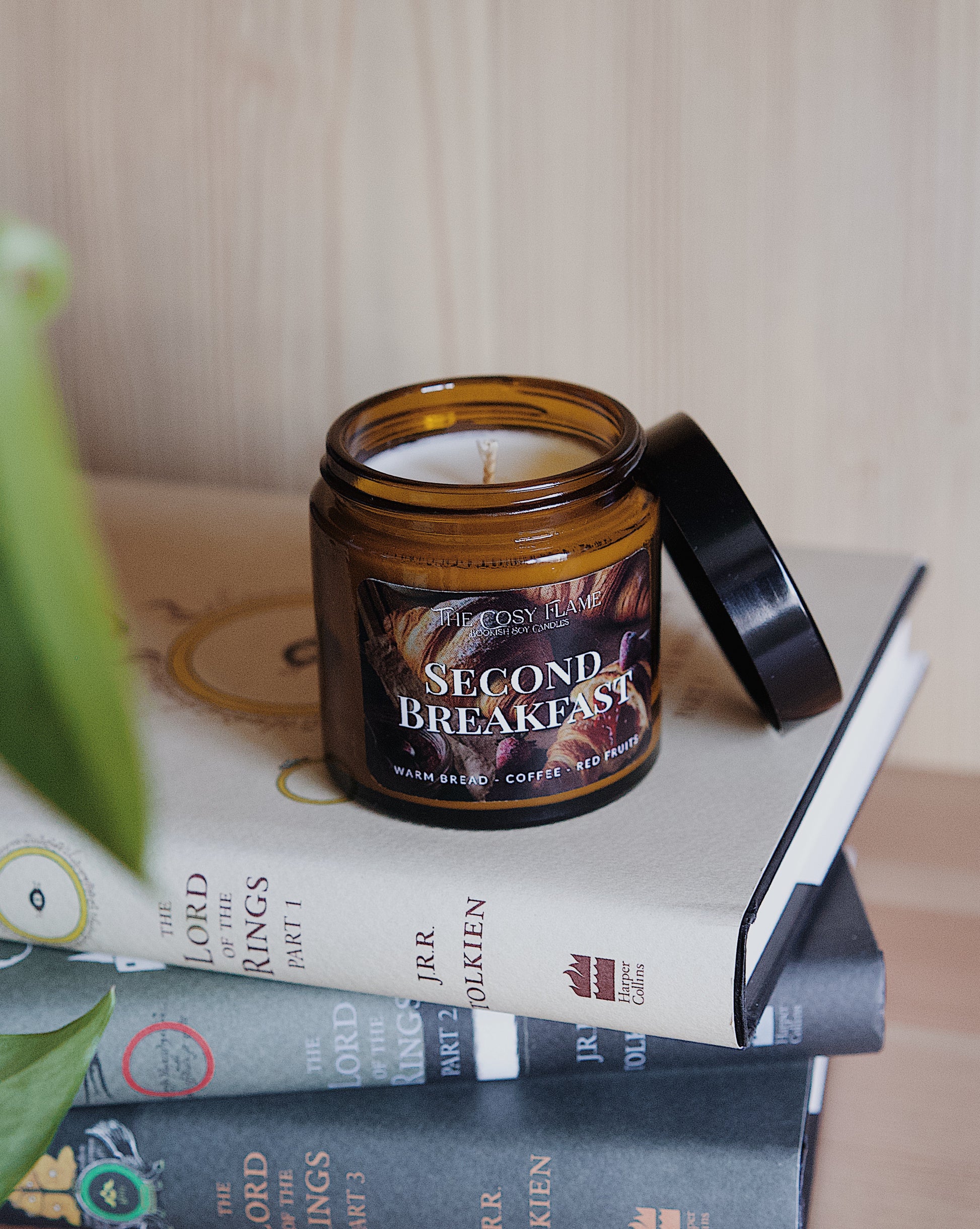 Amber glass candle jar labelled ‘Second Breakfast’ from The Cosy Flame, scented with warm bread, coffee and red fruits, and The Lord of the Rings books in the background.