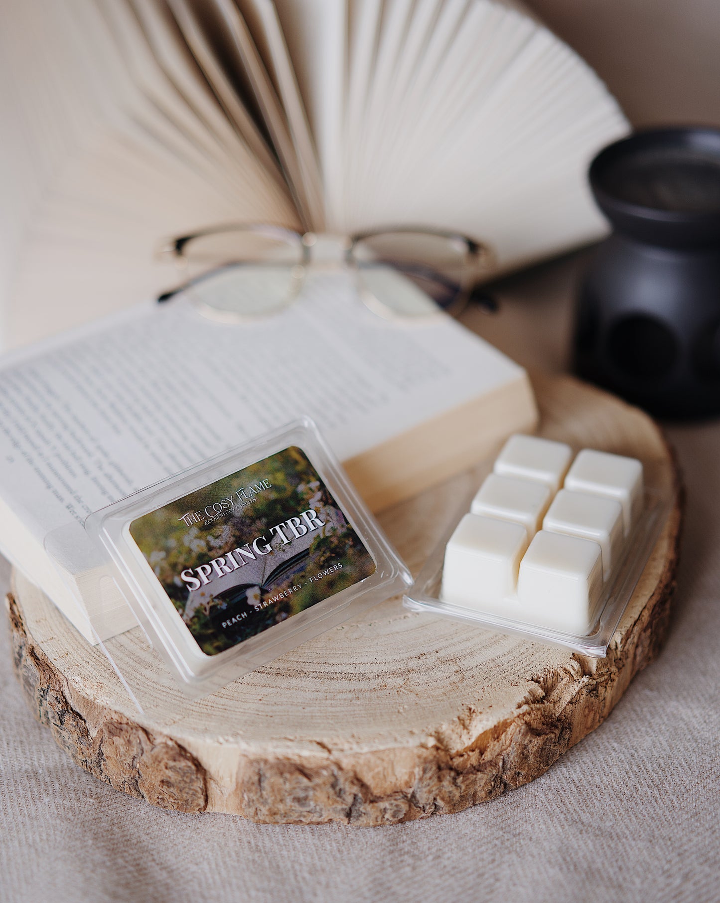Spring TBR soy wax melts by The Cosy Flame, featuring peach, strawberry and flowers scent notes, displayed on a wooden slice beside an open book and glasses.