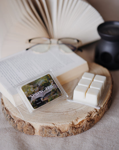 Spring TBR soy wax melts by The Cosy Flame, featuring peach, strawberry and flowers scent notes, displayed on a wooden slice beside an open book and glasses.