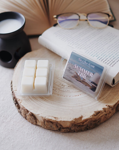 Summer TBR soy wax melts by The Cosy Flame, featuring pineapple and coconut scent notes, displayed on a wooden slice beside an open book and glasses.