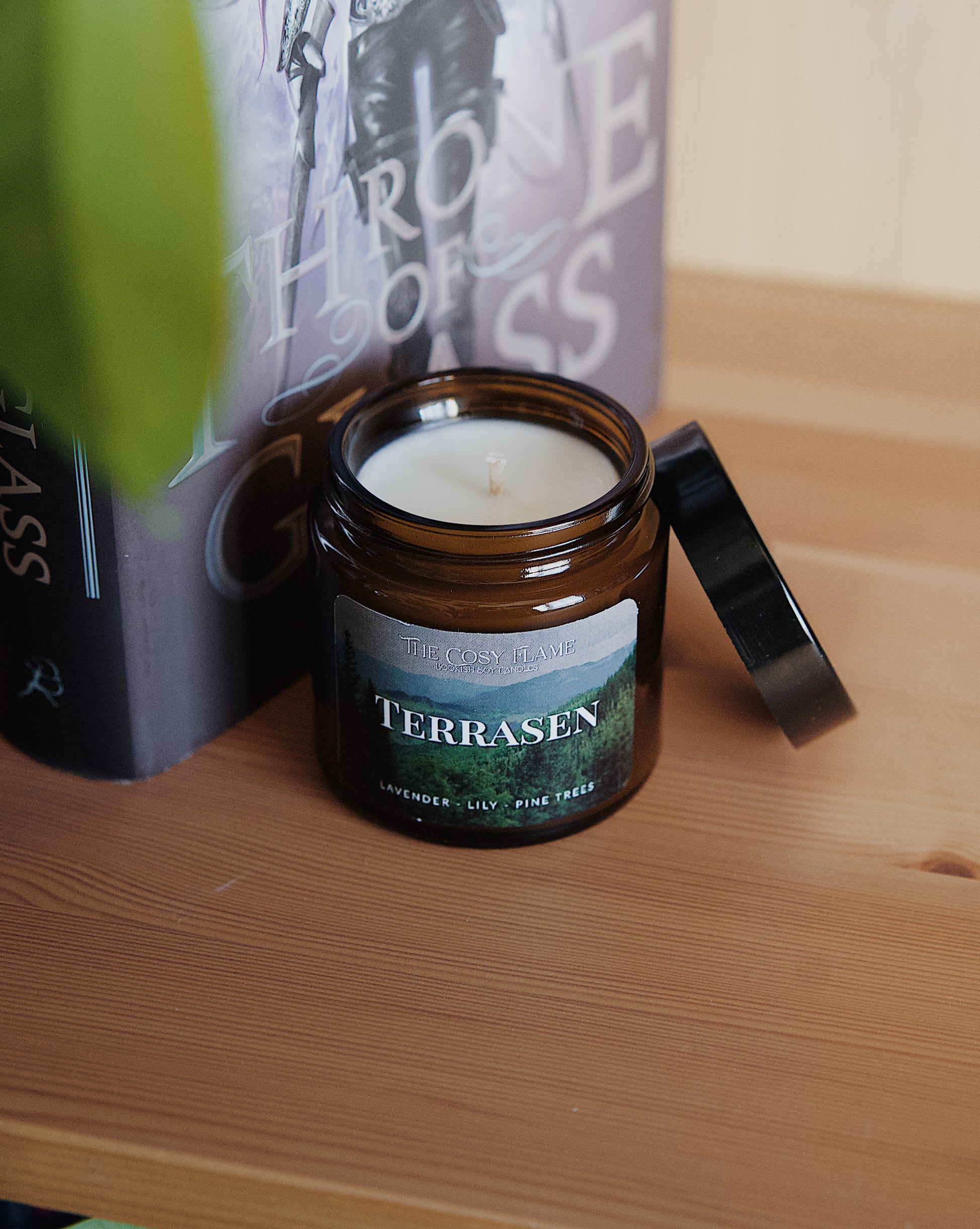 Amber glass candle jar labelled ‘Terrasen’ from The Cosy Flame, scented with lavender, lily and pine trees, and Throne of Glass book in the background.