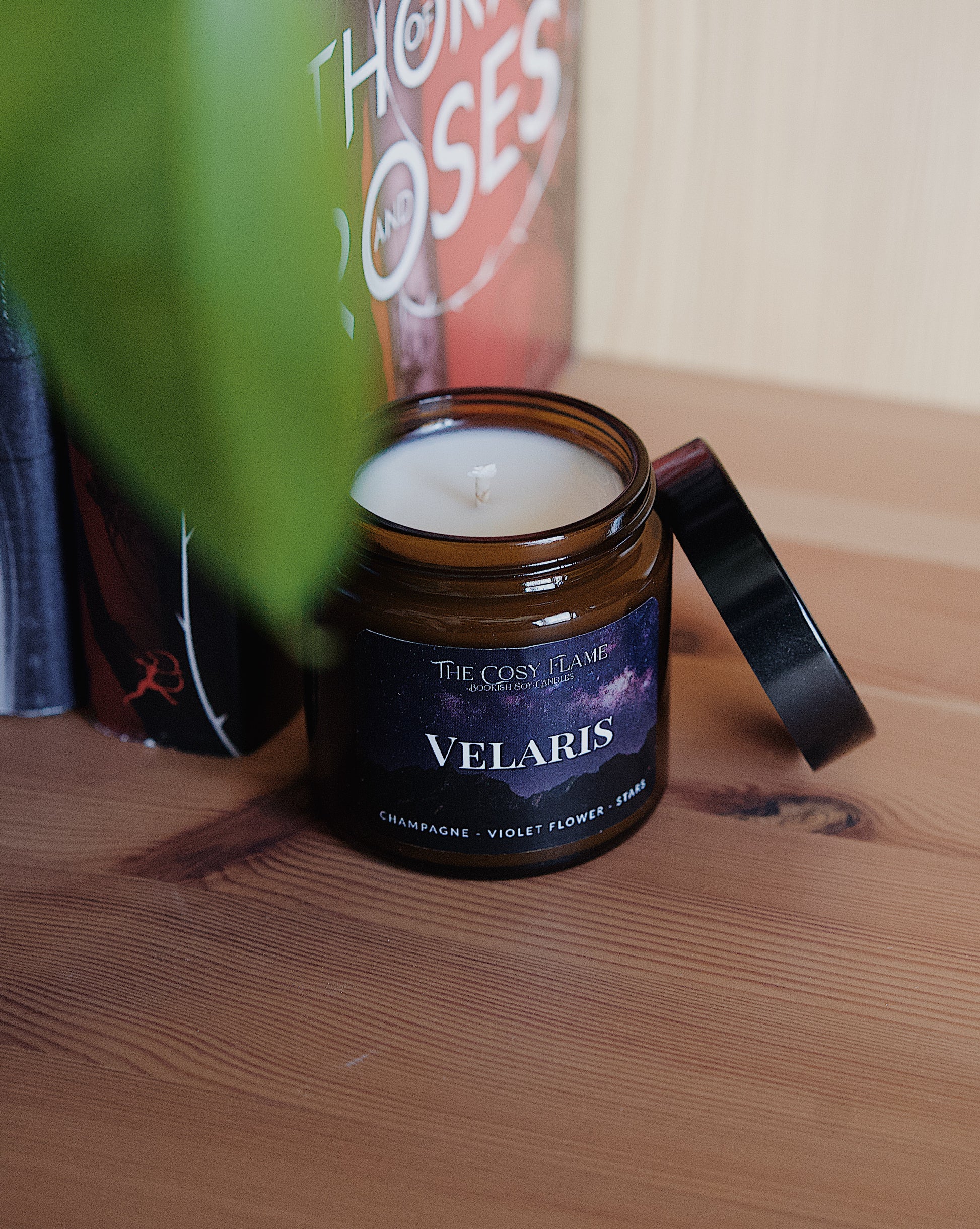 Amber glass candle jar labelled ‘Velaris’ from The Cosy Flame, scented with champagne and violet flower, and A Court of Thorns and Roses books in the background.