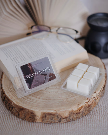Winter TBR soy wax melts by The Cosy Flame, featuring frosted berries and orange scent notes, displayed on a wooden slice beside an open book and glasses.