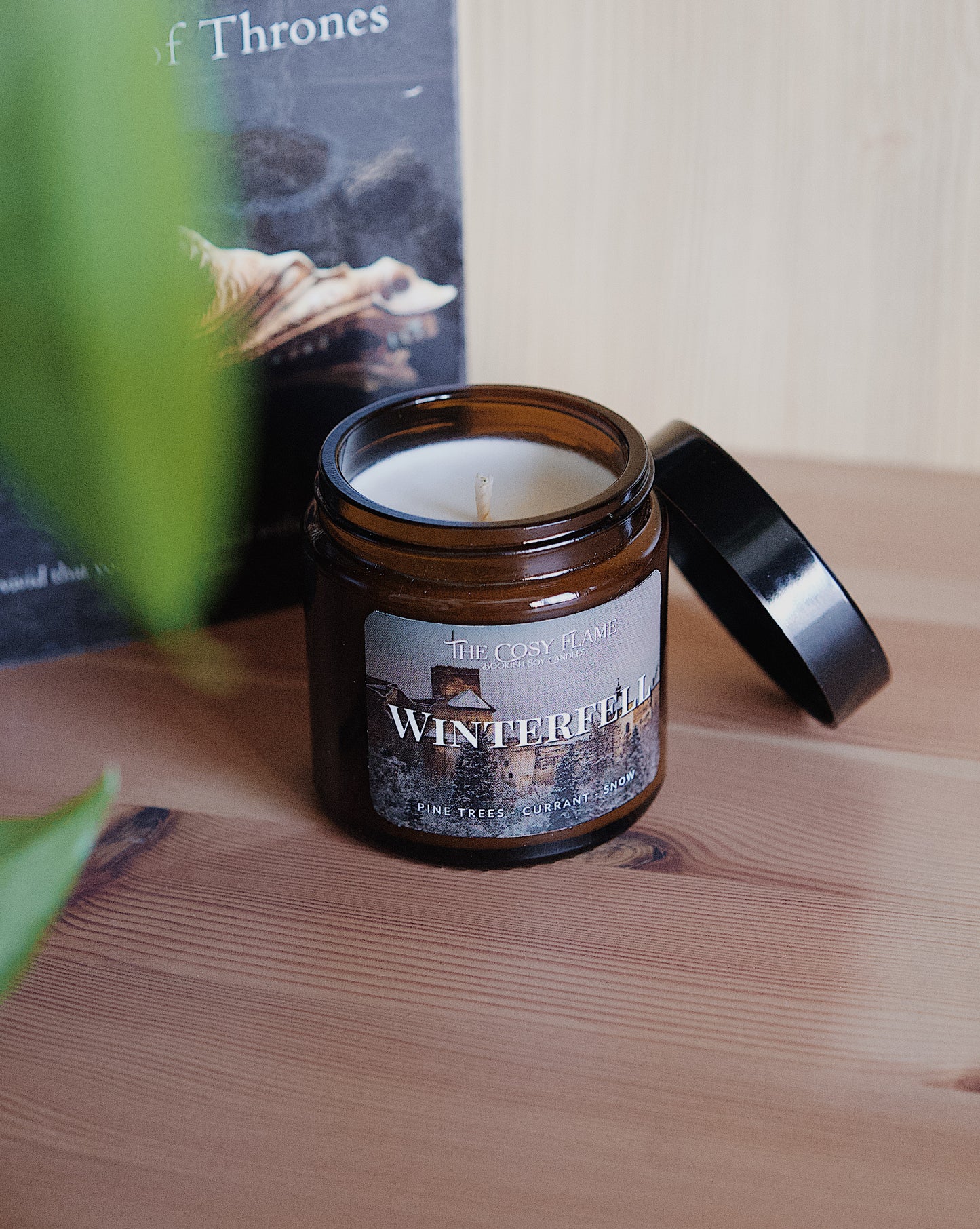 Amber glass candle jar labelled ‘Winterfell’ from The Cosy Flame, scented with pine trees and currant, and Game of Thrones book in the background.